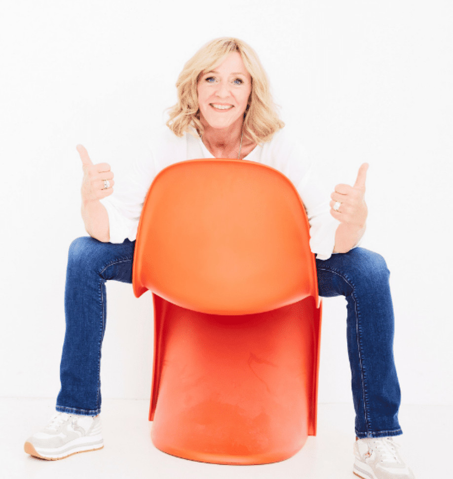 Das Bild zeigt Gabrielle, eine Dipl. Heilpädagogin, die in einem orangefarbenen Plastikstuhl sitzt. Sie hat eine aufrechte Haltung und hält den Daumen hoch, was auf eine positive und optimistische Einstellung hinweist. Möglicherweise soll das Bild Gabrielle als sympathische und professionelle Heilpädagogin darstellen, die ihren Kunden hilft, ihre Ziele zu erreichen und positive Veränderungen in ihrem Leben zu schaffen.